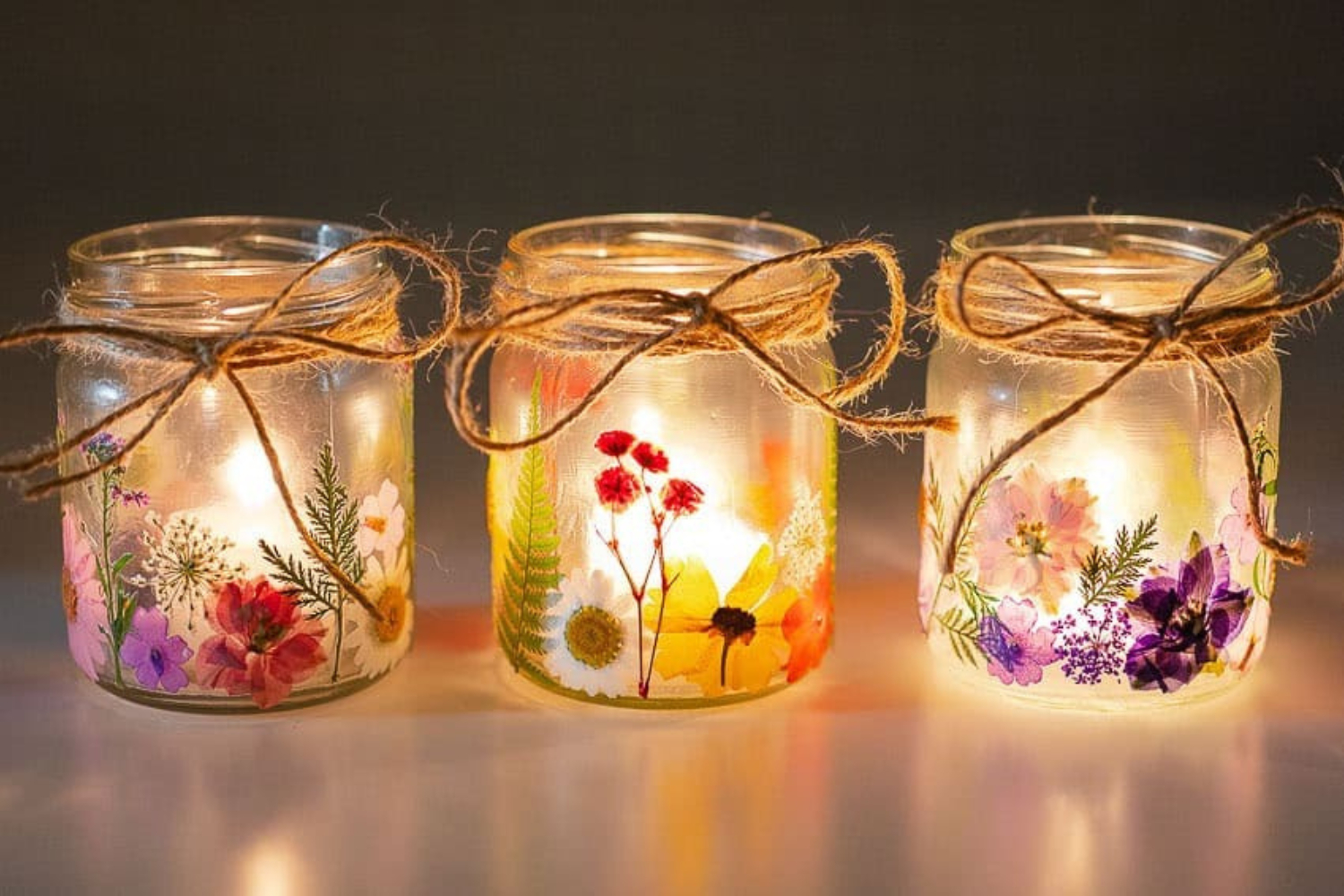 three glass jars with pressed flowers and candles inside