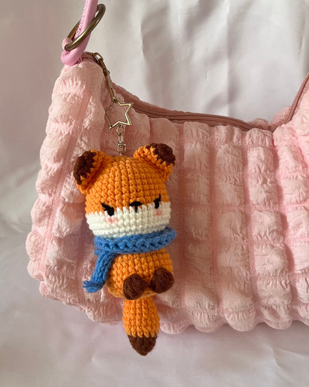 Cozy Amigurumi Fox: A pocket-sized crocheted amigurumi fox with a tiny, bright blue scarf wrapped around its neck